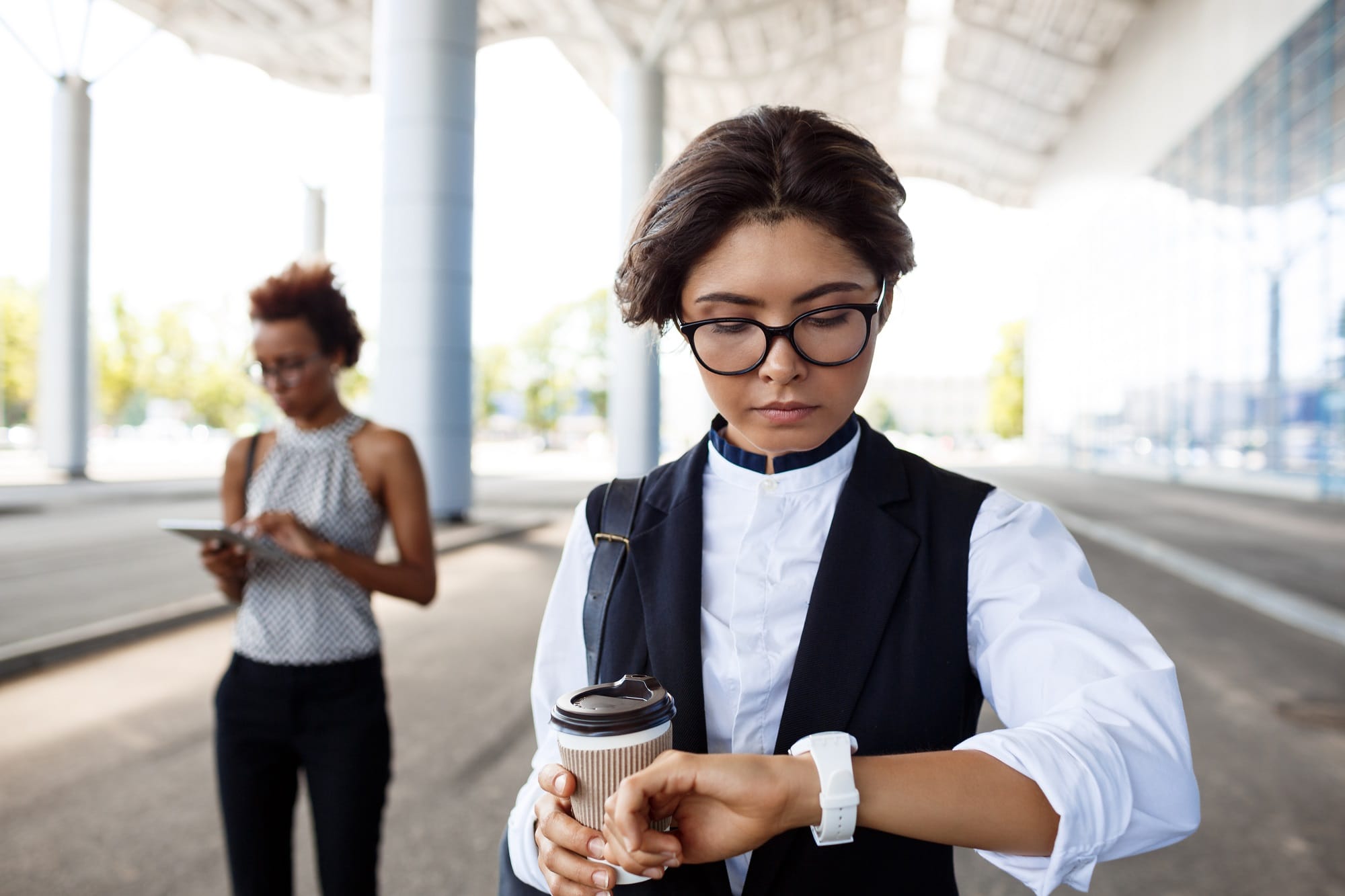 Pengusaha wanita berkacamata memegang kopi sambil melihat jam tangan di area bisnis